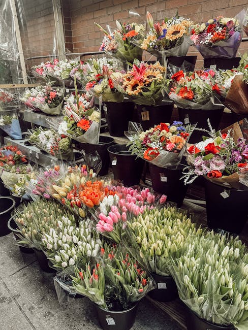 A display of various fresh flower bouquets arranged on black plastic buckets and shelves inside a flower shop, exhibiting a variety of vibrant floral arrangements. The bouquets feature a mix of flower